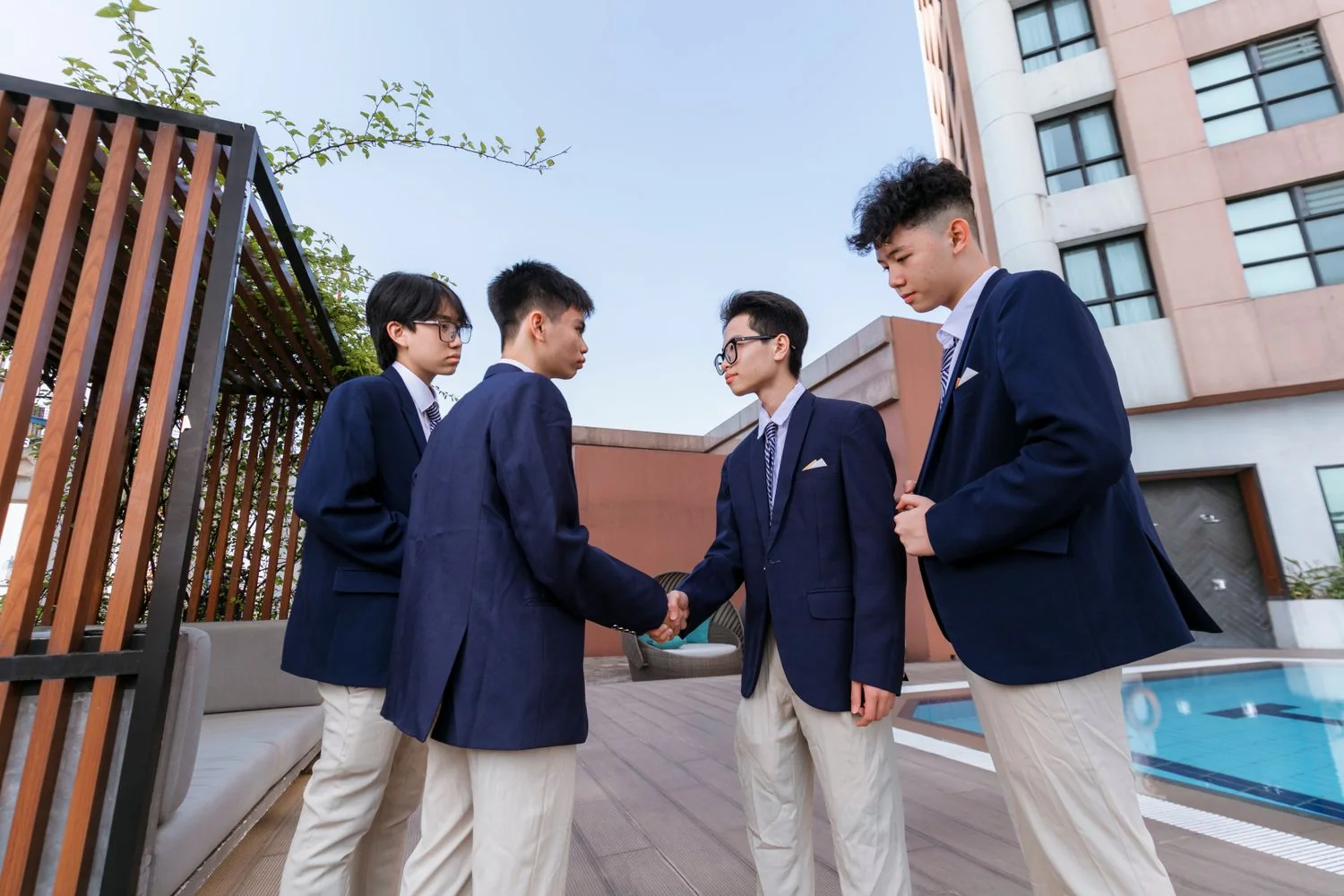 Four teenagers in navy blazers and striped ties outside a modern building